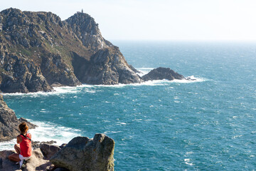 Woman sitting on rocky cliffs enjoying the Atlantic Ocean landscape from Alto do Príncipe viewpoint in the Cíes Islands, part of the Atlantic Islands of Galicia National Park in Galicia, Spain. © Fominayaphoto