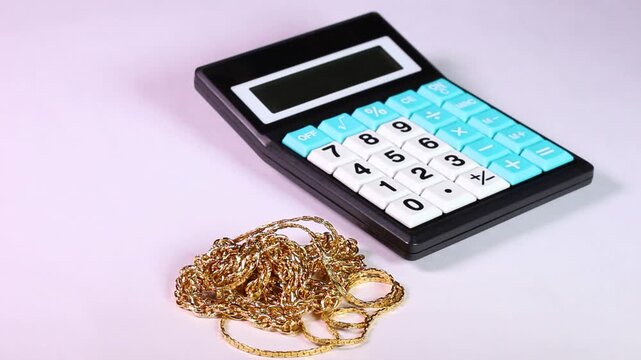 白背景で回転する電卓とゴールドジュエリー