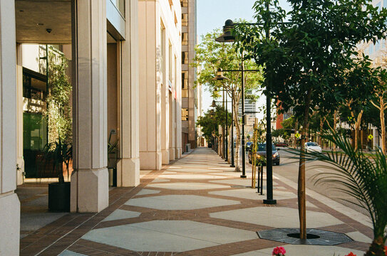 Sunny urban sidewalk in Glendale, California with modern buildings, street lamps and trees creating strong geometric shadows. Calm city street scene with contemporary architecture and clean pedestrian