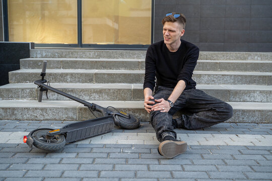 Young man in pain, fallen of the electric scoter injuring his leg and knee