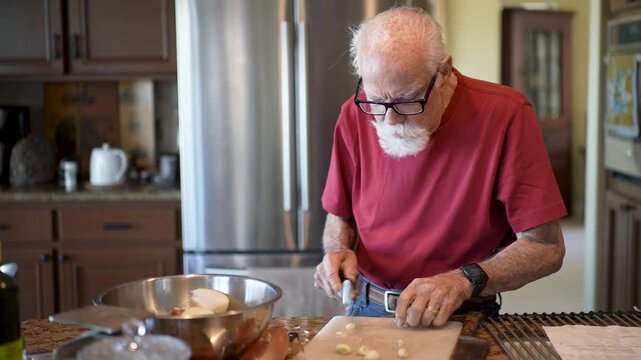 Senior man mashes garlic cloves in his kitchen as he follows a recipe for a meal preparation.