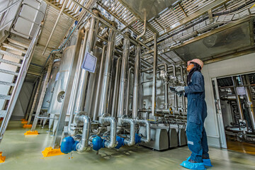 Fototapeta premium Male work inspection process stainless steel tanks and pipe with a pressure meter in the equipment tank facility for the drink cellar with a vertical