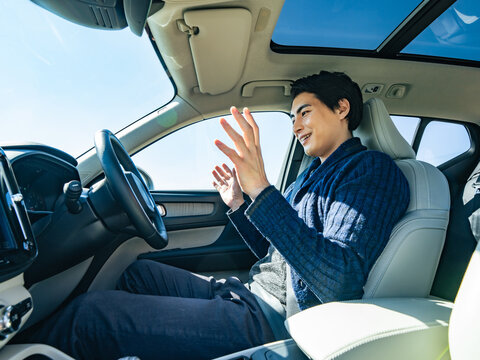 自動車の運転席でハンズフリー運転する男性ドライバー