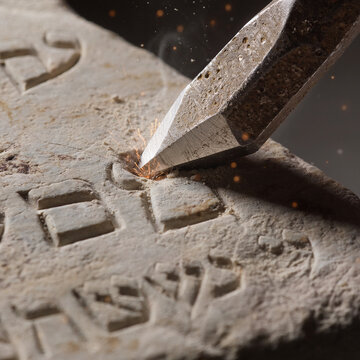 Macro of hand carving ancient hebrew into stone tablet