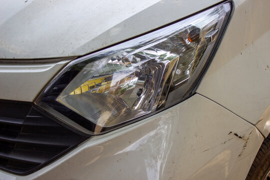 Jakarta, Indonesia - March 16 2026: Left headlight of a white Daihatsu Sigra car with scratches on the body near the front bumper.