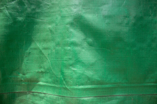 Green plastic tarpaulin with a coarse woven texture and a wrinkled surface.