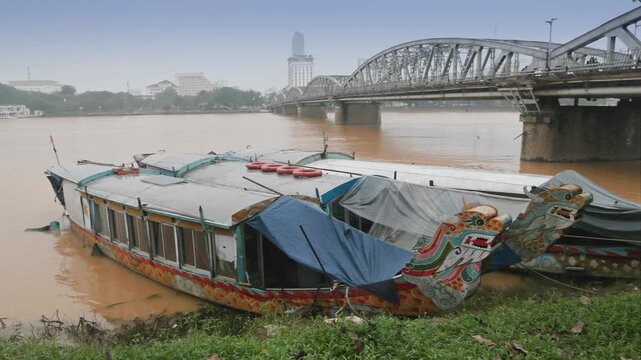 Dragon boats sit on the muddy banks of the Perfume River in Hue, Vietnam. The boats are docked near the Truong Tien Bridge, awaiting tourists for river tours.