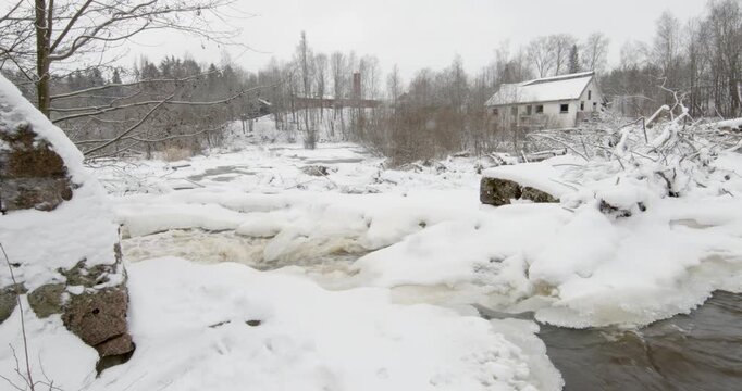 Vantaankoski rapids during the winter. The white building visible on the of the river is the Vantaankoski old mill in cloudy winter weather, Vantaa, Finland, Europe.