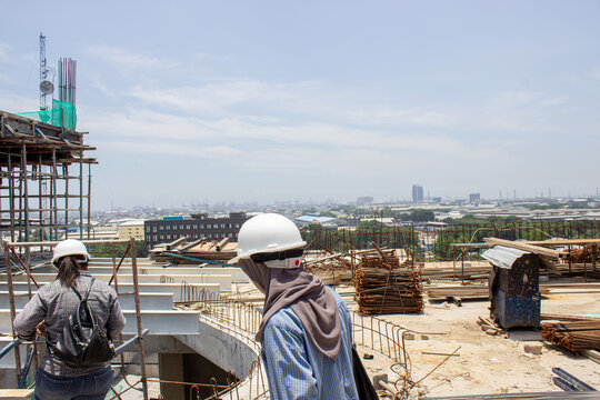 Jakarta, Indonesia - March 16 2026: Construction workers wearing safety helmets on top of a building overlooking the city view of Jakarta from a height