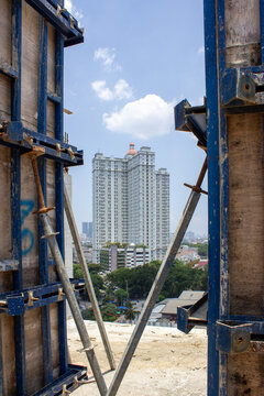 View of a high-rise apartment building with an orange dome seen through the metal scaffolding gap at a construction project site in Jakarta