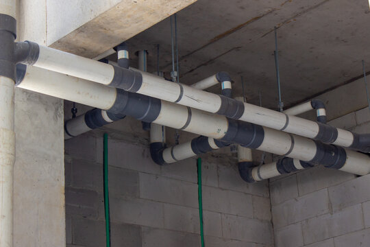 Installation of white PVC pipes and grey fittings mounted on a concrete ceiling inside a building under construction