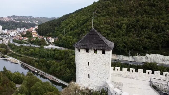 Medieval cliff-top fortress overlooking river and red-roofed town in Uzice, Serbia, with winding road. g.