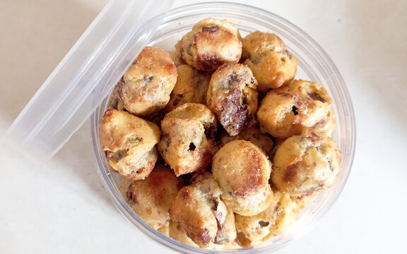 Top view of homemade mini chocolate ball pastries stored in a transparent plastic container. These small baked snacks have a golden brown texture with visible chocolate filling inside, commonly served