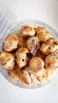 Top view of homemade mini chocolate ball pastries stored in a transparent plastic container. These small baked snacks have a golden brown texture with visible chocolate filling inside, commonly served