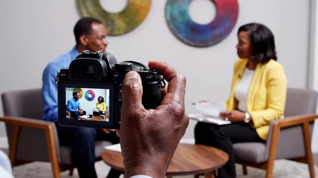 Camera capturing interview with man and woman sitting on chairs
