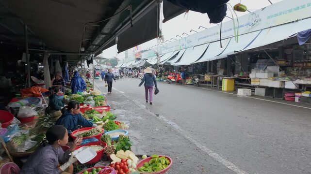 HUE, VIETNAM &ndash; 22 November 2025: Vendors prepare and sell fresh produce at a local market in Dong Ba Market. A shopper walks along the street.