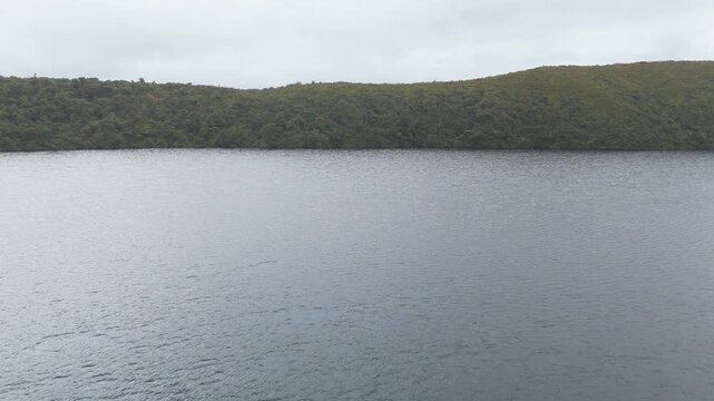 A serene view of the calm lagoon water reflecting green hills under overcast skies, showcasing tranquility in nature.