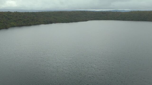 A serene view of the calm lagoon water reflecting green hills under overcast skies, showcasing tranquility in nature.