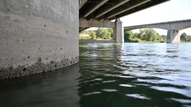 Close up view of concrete bridge pillar base at water level with another bridge in background.