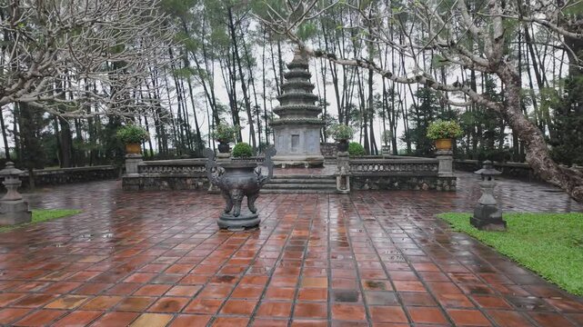 A serene view of the tranquil garden with its bare trees, pagoda, and tiled walkways after a rain shower. Thien Mu Pagoda, Hue, Vietnam.