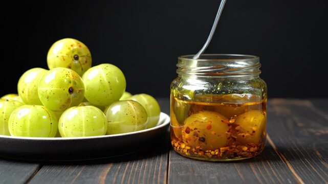 Indian Gooseberry Amla Pickle in Glass Jar with Raw Fruits on Wooden Table for Healthy Traditional Food