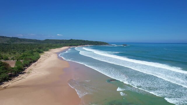 Aerial drone footage of Pulau Manuk beach, in Banten, Java island, Indonesia, with beautiful white sand, blue sea waters, waves for surfing, and forests behind, on the way to the famous Sawarna beach