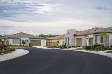New construction single-family homes along a curved residential street in a modern suburban housing development. Planned neighborhood with contemporary architecture representing suburban. © Alex