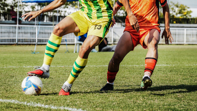 Close up sports action of football players competing for control of the ball on green field, highlighting powerful legs, athletic performance, outdoor competition