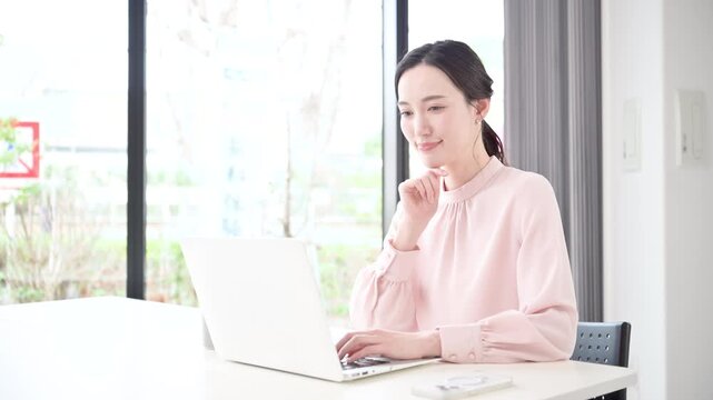 デスクで座るパソコンの仕事をするピンクの服を着た綺麗な女性の動画　キャリアウーマンなどの働く女性イメージ