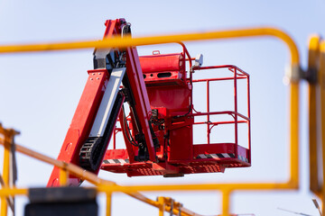 Mobile boom lift basket and red hydraulic arm within a construction equipment yard, representing access technology, service work and rental industry © K