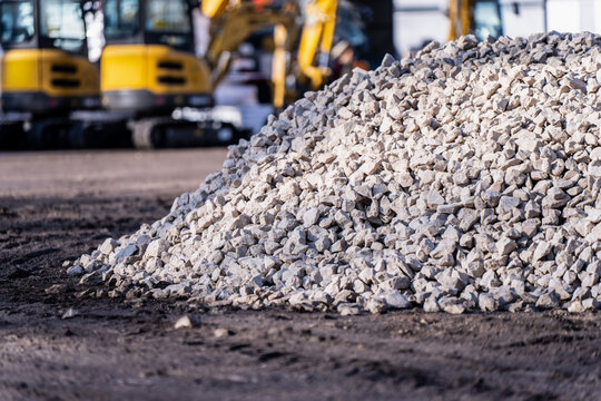 Heap of light gravel at an active worksite with heavy machinery behind, representing aggregate supply, construction logistics and ground preparation