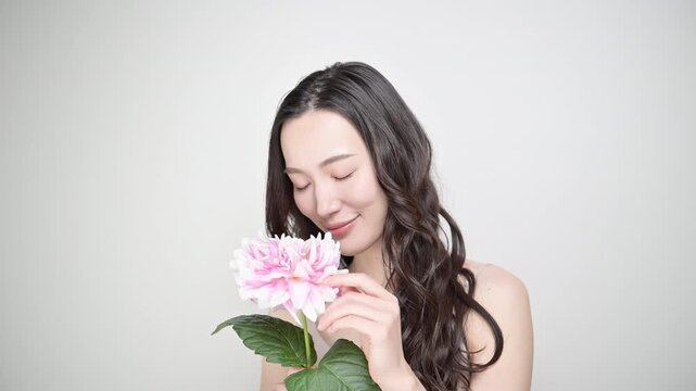 A beauty image of a woman radiating happiness, holding a dahlia flower against a white background, evoking a pink springtime vibe