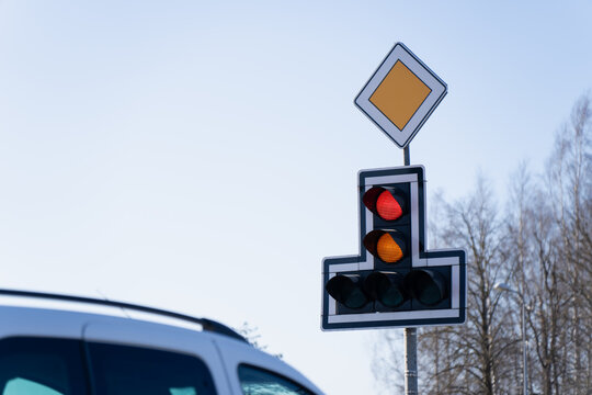 Priority road sign above a traffic signal with red and amber lights, representing intersection control, driving regulation and street safety