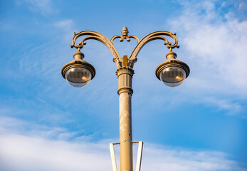 Ornate vintage street lamp illuminating city streets under a clear blue sky
