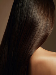 Fototapeta premium Close up of a woman from behind showing her long, shiny dark brunette hair and smooth shoulder.
