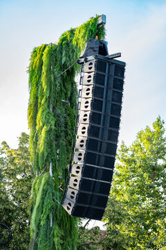 Line array speaker system hanging on a plant-covered column at an outdoor event