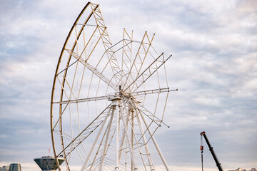 Ferris wheel structure under construction, steel frame rising into the cloudy sky
