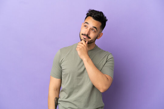 Young caucasian man isolated on purple background and looking up