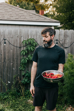 Man holds colander full of freshly harvested fruits and vegetables
