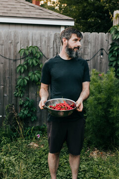 Man holds colander full of freshly harvested fruits and vegetables