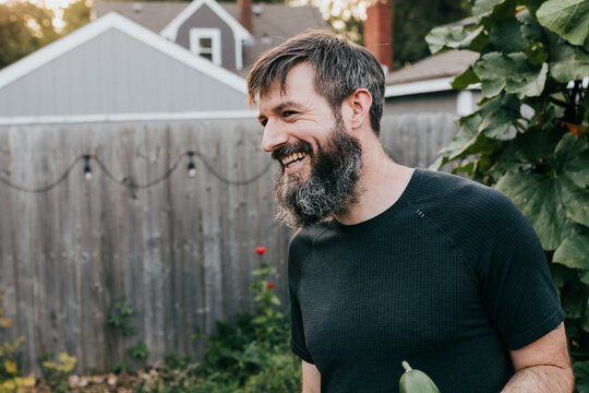 Man faces the left while smiling in backyard garden on Fall evening