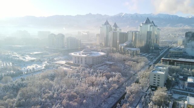 A breathtaking cinematic drone flight over the upper part of Almaty, Kazakhstan, following a massive winter snowfall. The footage features slow, majestic panoramic sweeps across the city's skyline, sh