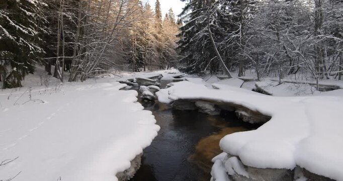 Tranquil, partially frozen river flowing through a snow-covered forest during winter, Matarinkoski, Vantaa, Finland, Europe.