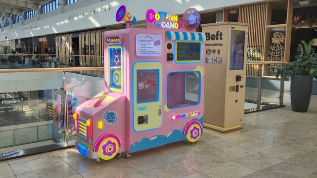 Vilnius Lithuania - 05.03.2026, pastel pink cotton candy vending machine with neon trim beside Boft photo printing kiosk in a bright shopping mall corridor under skylights