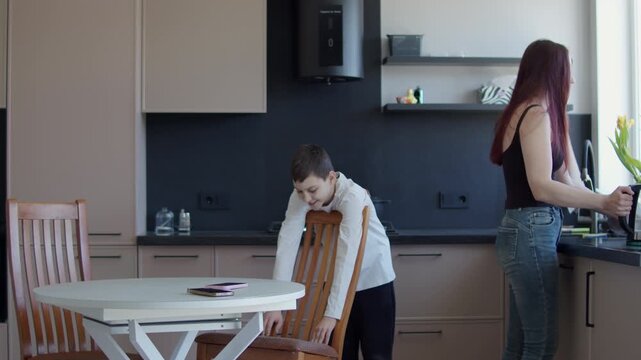 Mother preparing food in kitchen while tired boy leaning on chair