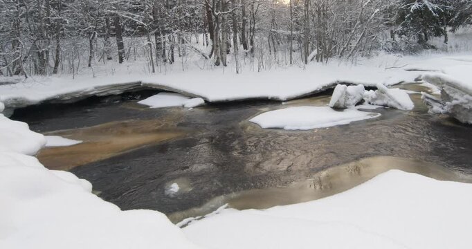 Tranquil, partially frozen river flowing through a snow-covered forest during winter, Matarinkoski, Vantaa, Finland, Europe.
