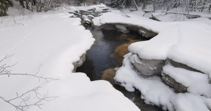 Tranquil, partially frozen river flowing through a snow-covered forest during winter, Matarinkoski, Vantaa, Finland, Europe.