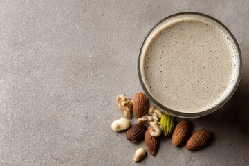 Close up overhead view of a glass of creamy almond milk beverage scattered with various whole nuts including almonds walnuts and macadamia nuts on a textured grey background with soft natural light
