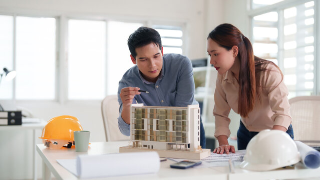 Asian adult male architect female engineer discuss building model design blueprints office workspace professional project planning construction development infrastructure