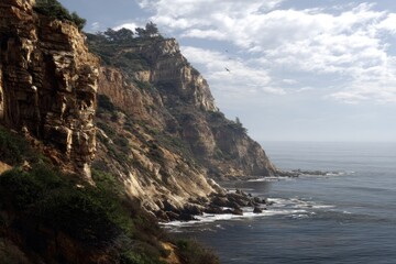 Coastal scene rocky cliffs cascade to meet ocean under a partly cloudy sky